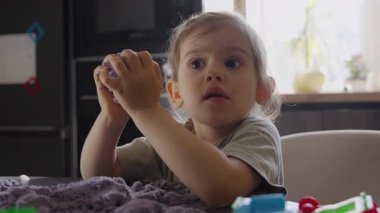 Genç kız küresel oyuncağı dikkatle izler, beyaz kız güneşli nesnelere yoğunlaşır.