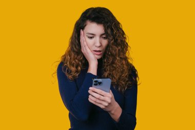 Bir kadın, sosyal medya ve iletişim temaları için ideal telefonuna bakarken şaşırmış bir ifade sergiliyor.