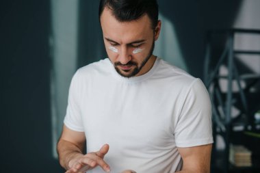 Konforlu bir evde yaşayan bir adam cilt bakımı ürünleri uyguluyor, modern yaşam tarzı seçimlerini ve kişisel bakım alışkanlıklarını yansıtıyor.