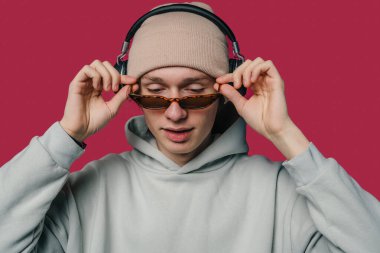 Modayı takip eden genç bir birey, canlı bir arka plana karşı kulaklık takarken şık güneş gözlüğü takıyor.