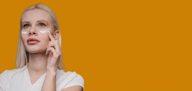 Dikkatli bir şekilde göz kremi süren bir kadın, sağlıklı cildine çağdaş cilt bakımını gösteriyor.