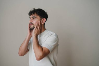 Tarafsız stüdyo ortamında cilt bakımı sırasında duygusal tepki gösteren bir adamın gizli bir fotoğrafı.