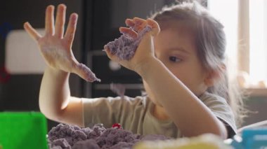 Bir çocuk, yaratıcılığını ve duyusal keşiflerini arttıran renkli, esnek kinetik kumla mutlu bir şekilde meşgul olur.