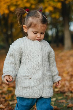Çocuk yaprağı inceliyor, yere bakan, çökmüş gözleri olan düşünceli bir çocuk örgü süveterler ve açık havada düşen yapraklar arasında.