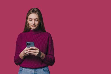 Stüdyo ortamında akıllı telefonuyla mesajları kaydırırken sıradan giyinmiş bir kadın konsantre oluyor.