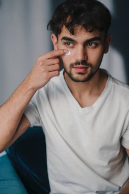 Fotoşoptan önce göz teması kuran genç adam fotoğraf çekimi hazırlıkları sırasında göz kapağını kontrol eder.