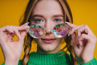 Çiçekli güneş gözlüğü ve parlak sarı arka planda neşeli bir ifade sergileyen moda meraklısı.