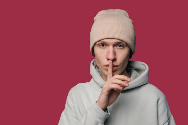 Sessiz ruh halini gösteren parmakları olan genç bir birey, sakin bir ortamda sessizliğini neşeli bir şekilde taşır.