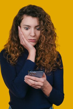 Kıvırcık saçlı bir kadın cep telefonundan zaman duyarlı uyarıyı okuduğunda şok geçiriyor.