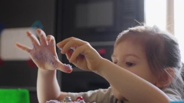 Yapışkan mor maddeyi inceleyen genç kız, küçük çocuk yapışkan menekşe hamurunu parmaklarıyla keşfediyor.