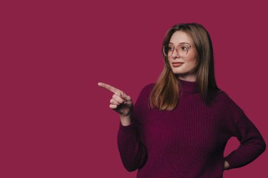 Gözlükle, bordo süveterle ve düşünceli ifadeyle, sınıf ya da sunumla sağı gösteren beyaz bir kadın.