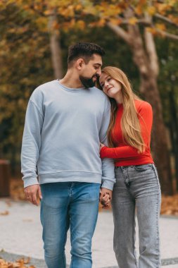 Hassas bir anda çift alın dokunuşu, yakın göz teması, yumuşak vücut dili, sessiz kot pantolon ile kırmızı kazak kontrastı.