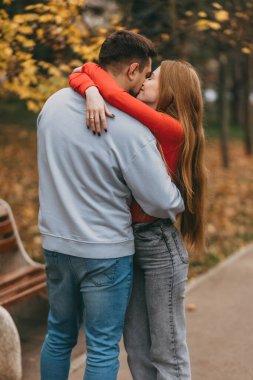 Parkta kucaklaşan beyaz bir çift, sıcak bir kucaklama, sonbahar yeşilliği, hakiki rahatlık