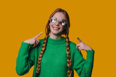 Örgü, papatya güneş gözlüğü, yeşil süveter, retro hardal arkaplan, parlak bir tuhaflık.