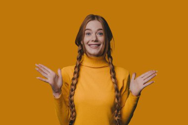 Genç beyaz kadın avuçlarını hardal kaplamasına karşı açık tutuyor. Sarı balıkçı yaka ve örgülü saç nakli