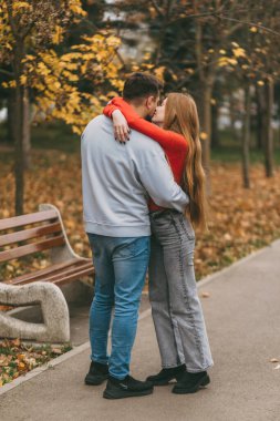 çift yolda yürürken sarılıyor, bank ve altın yapraklar astarlı yürüyüş yolu, gündelik kot ve yumuşak