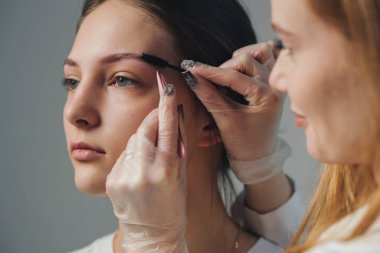 estetisyen kaş bölgesinde eldiven ve pigmentle hassas mikro patinaj yapıyor.,