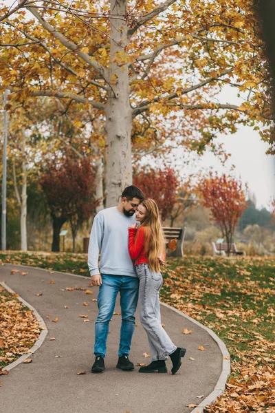 Sonbahar ağaçlarıyla kaplı yolda el ele yürüyen çift yaprakları dökülmüş ve şehir parkının havası kırmızı.