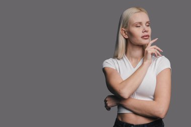 Kollarını çapraz yapmış, gözleri kapalı, beyaz tişört ve siyah kot pantolon giymiş bir kadının stüdyo portresi.