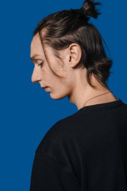 Mavi arka planda derin derin düşüncelere dalan, saçlarını bağlamış, cilt dokusu ve çene çizgisi olan, yumuşak stüdyo.