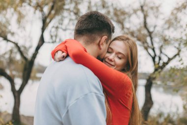 Kapalı gökyüzü altında mevsimlik renklerle çevrili çiftlerin kucaklaştığı sahneler.