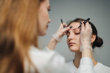 Yandan bakan makyaj sanatçısı kadın müşteriye kaş şekli, dikkatle muayene ve ölçüm yapıyor.