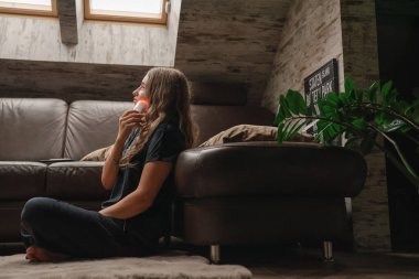 Genç bir kadın kanepenin yanında oturuyor ve pencereye bakıyor. Tavan penceresi ışıldıyor. Doğal ışık kalıpları