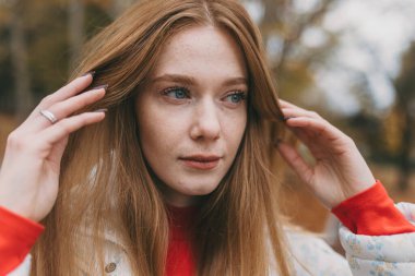 Kapalı alanda saçları ayarlayan genç bir kadın, yumuşak sonbahar ışığı, çilli düşünceli bir ifade.