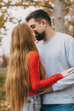 Samimi sonbahar parkı beyaz çifti kucaklıyor. Alnından öpücükler, uzun kızıl saçlar, kot pantolon ve rahat bir süveter.,