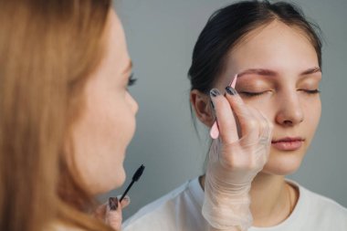 Makyajcı, eldivenli elleri olan müşteriye göz makyajı yapıyor. Göz kapağında hassas fırça darbeleri, pigment.