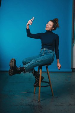 Beyaz kadın sözü geçen, mavi stüdyoda kot pantolon ve balıkçı yaka kazak giyen, selfie çeken biri.