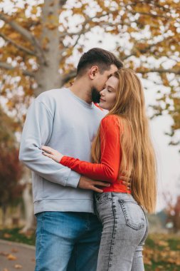 Alnıyla sarılan çift altın ağaçların altına dokunuyor. Sessiz yakınlık, yumuşak göz teması, sıcak örgü.