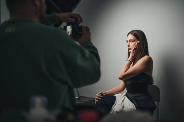 Dramatik tek kaynaklı ışık altında oturan modelle stüdyo portresi oturumu, fotoğrafçı çerçeveli çekim