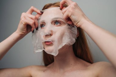 Kızıl saçlı, hidrasyon için maske takıyor ve kişisel bakım anında parıldıyor. Eller pürüzsüz seruma batırılmış