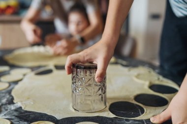 Un kaplı tezgahta cam ile kurabiye hamuru kesen yakın plan eller, dairesel kesikler ve eğlenceli doku,