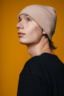 Bereli genç adam yukarı bakıyor, stüdyo portresi sıcak hardal arkaplan, karamsar yan aydınlatma, yün dokusu, dalgın