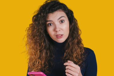 Şaşkın bir kadın pembe bir telefon tutuyor. Beklenmedik mesajlar okuyor. Gözleri açık ve kaşlarını kaldırmış.