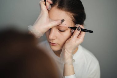 yakın plan beyaz kadın kaşları kalem hatlarıyla eşleşiyor, teknisyen kemeri sabit elle işaretliyor.,