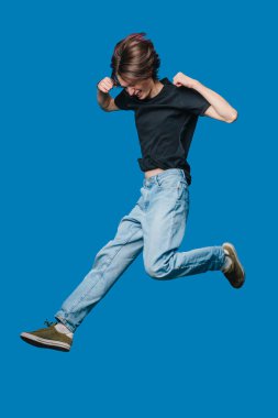 Yumruklarla Sıçrayan Enerjik İnsan Mavi Stüdyo Arkaplanına Karşı Zafer İfadesi, Sıradan Kot