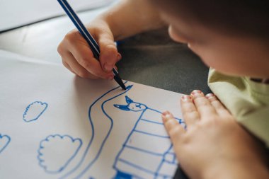 Kağıt üzerinde mavi işaretli çocuk, kalın çizgiler ev ve bulut şekillendirme, konsantre küçük eller rehberliği