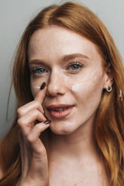 Yakın plan kızıl saçlının burnuna dokunması çilleri ve minimum makyajı gösteriyor. Stüdyoda düşünceli ifadesi olan test noktası serumu.