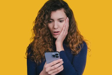 Kadın telefon mesajını okurken şaşırdı, şok olmuş yüz yüze sarı arka plan, samimi tepki