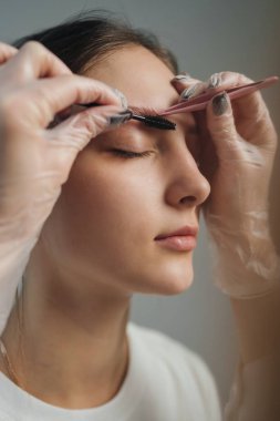 Yakın plan eldivenli eller cımbızla kaş şekillendirme, sabit hassasiyet ve odaklanmış hareket, metal alet ve küçük fırça detayı,