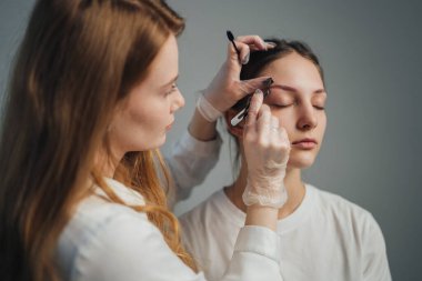 Kaş teknisyeni müşterinin kaşlarını tam olarak şekillendiriyor, eldiven takıyor ve mikro patenli kalem ve cımbız kullanıyor.