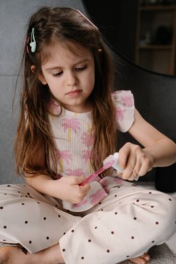 Genç beyaz kız otururken çarşaftan çıkartma soyuyor, odaklanmış eller, nazik konsantrasyon, yumuşak giysi,