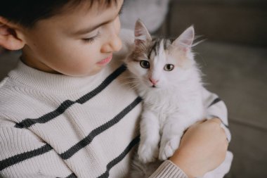 Genç beyaz çocuk beşikte tüylü kedi, koruyucu duruş ve sabit bakış, yumuşak dokular, sakin ev içi, nazik iç mekan