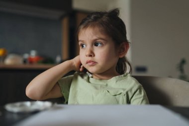 Sıcak mutfak ortamında yemek yerken düşünceli bir çocuk aile yemek masasında sessizce oturuyor.