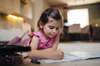 Genç kız evde resim malzemeleriyle mutlu bir boyama, parlak bir gülümseme ve odaklanmış vuruşlar, okuldan sonra eğlenceli bir oyun.