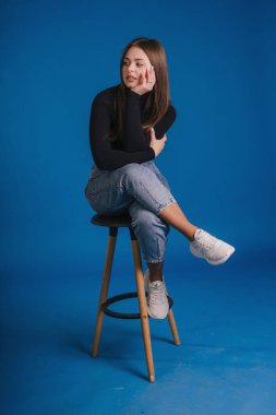 Taburede oturan, Düşünceli, Etnik Etkinlik Yaratıcı Danışmanı Siyah Balıkçı yaka giyen,