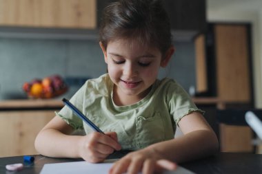 Masada çizim yapan genç bir kız, neşeli bir ifade, renkli kalemler ve kağıt, sıcak mutfak arka planı, rahatlamış.